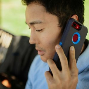 A young, Asian man sits on a bench outdoors, talking on a cell phone