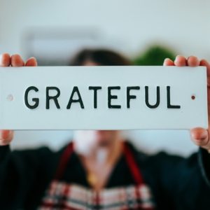 A person in an apron holds up a sign that says GRATEFUL over their face.