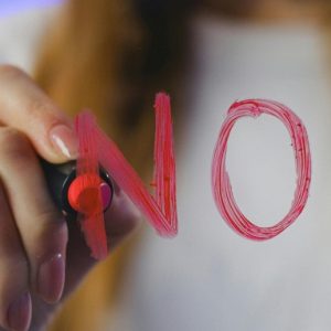 A woman writes the word "No!" on a clear surface in red lipstick.