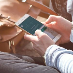 A person sits cross-legged outdoors, looking at the Monthly Health Check in their Workit Health app on a smartphone