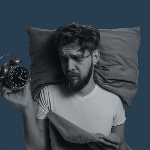 Sleepless man holding an alarm clock. Does alcohol cause insomnia?