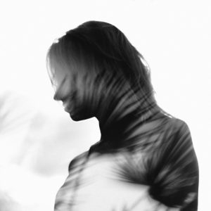 A double-exposure photo in which a woman's outline is overlaid with shadowy images of palm fronds.
