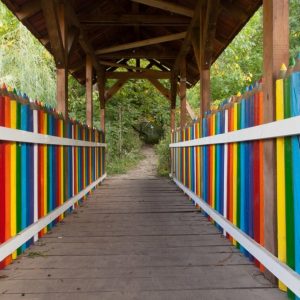 A covered bridge whose railings are shaped like colored pencils in rainbow colors.