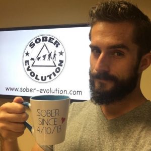 Austin Cooper of Sober Evolution holds a coffee mug that reads "Sober since 4/10/13"