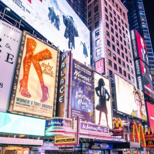 Broadway at night, lit up with signs for musicals and businesses.