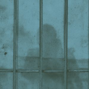 A concrete wall with metal bars in front of it, giving the impression of jail. The shadow of a woman falls across the bars and wall