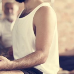 Several men in yoga clothing sit meditatively in lotus position