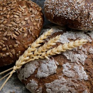 Three loaves of whole grain bread with a few stalks of wheat resting on top of them.