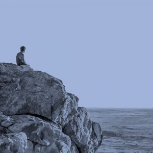 Sitting alone on a rock, looking at the ocean.