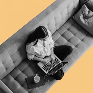 View from above of a woman on a sofa working on a laptop. Drinking while working from home