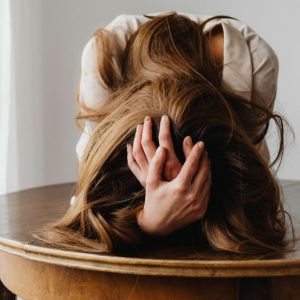 A woman slumps over a table with her head in her hands.