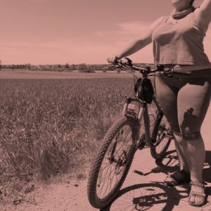 Peach overlay colors a black and white image of a woman standing next to her bicycle in a sunny field.