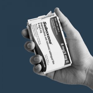 Hand holding a Suboxone box against a dark blue background