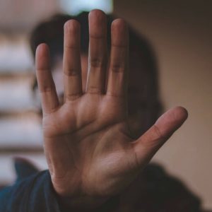 A person holding their hand up in the flat, palm-out gesture that means "stop."