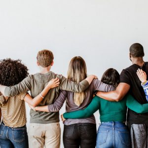 View from behind of a group of people standing side by side with their arms around one another. What's the point of recovery groups?