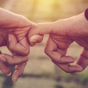 Closeup of holding hands by linking pinkies together.