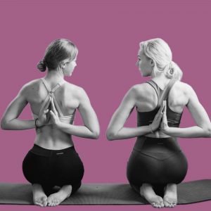 Two women kneel next to one another on mats, doing yoga