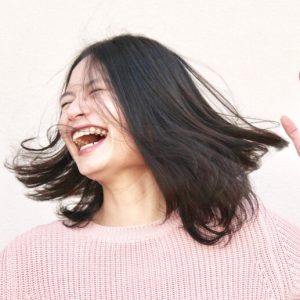 Young Asian woman laughs with her hands in the air and her hair swinging around her.