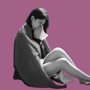 A woman wrapped in a blanket blowing her nose. Staying sober when you're sick.