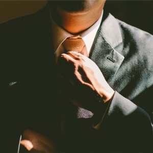 A man in a gray suit adjusts his tie