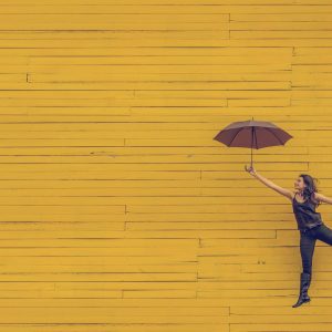 woman-jumping-with-umbrella-yellow-wall