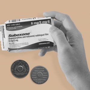 Hand holding a packet of Suboxone, with two sobriety chips in the background. Can Suboxone and the 12 steps work together?