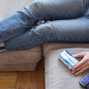 A person wearing blue jeans sits on a sofa with tehir legs stretched out in front of them, a box of Suboxone by their side.