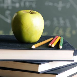 Green apple atop a stack of books on a desk. Addiction among teachers