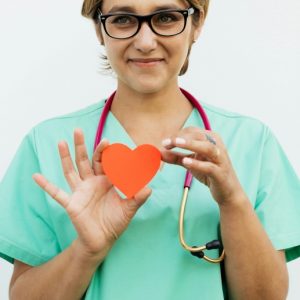 A female nurse in scrubs holds up a cheerful red heart