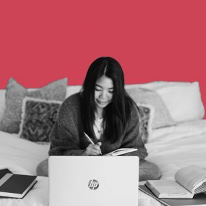 Woman sitting on the bed with a laptop and several open books around her