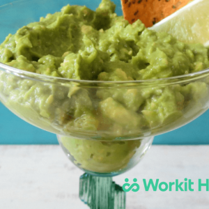 A margarita glass full of guacamole, garnished with lemon