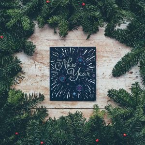 A hand-lettered sign reading "New Year" is surrounded by pine branches. Practical New Year's resolutions