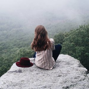 Photo of a woman sitting on a mountain looking at the view below