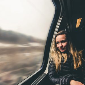 A blond woman on a train leans against the window, looking out