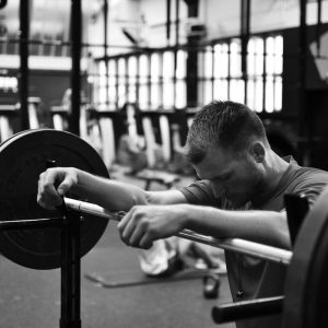 In a gym, a man leans his arms against a barbell loaded with weights