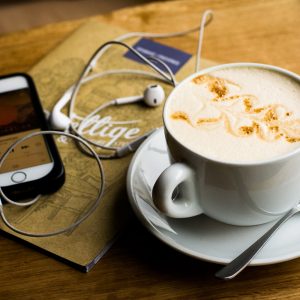 A latte next to an iPhone with earbuds. Recovery podcasts